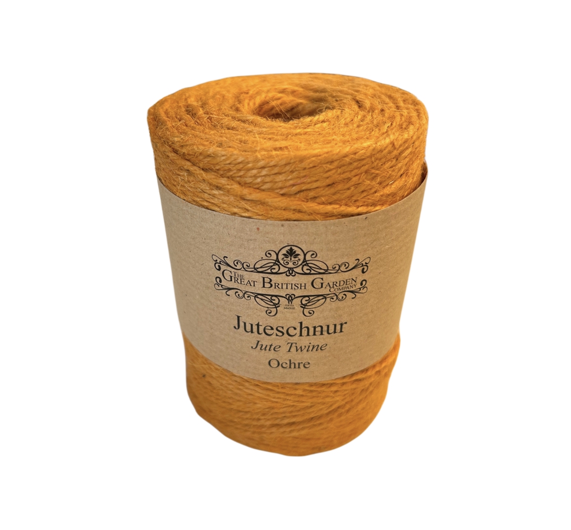 Hohe, zylindrische Rolle fest gewickelter Juteschnur in leuchtendem Ockergelb. Ein braunes Etikett mit „Great British Garden Company Juteschnur Jute Twine Ochre“ ist um die Mitte angebracht.