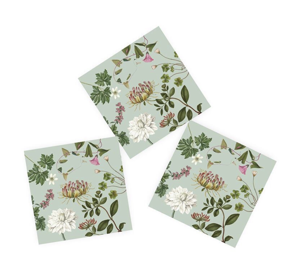 Drei dreilagige Papier-Servietten, diagonal auf weißer Fläche. Jede zeigt ein botanisches Flora Danica Motiv auf hellgrünem Grund: große gelb-rote Blüte, weiße chrysanthemenartige Blume, zarte rosa Blüten, grüne Blätter und Klee.