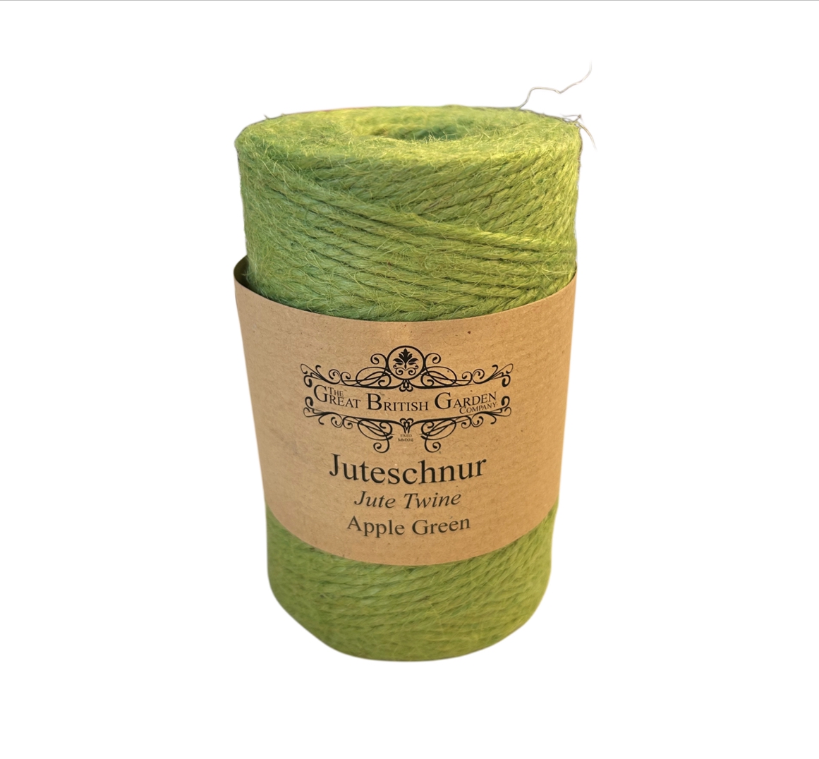 Stehende, zylindrische Rolle aus leuchtend apfelgrüner Juteschnur auf weißem Hintergrund. Braune Papierbanderole mit Logo "The Great British Garden Company" und Text "Juteschnur Jute Twine Apple Green" in der Mitte.